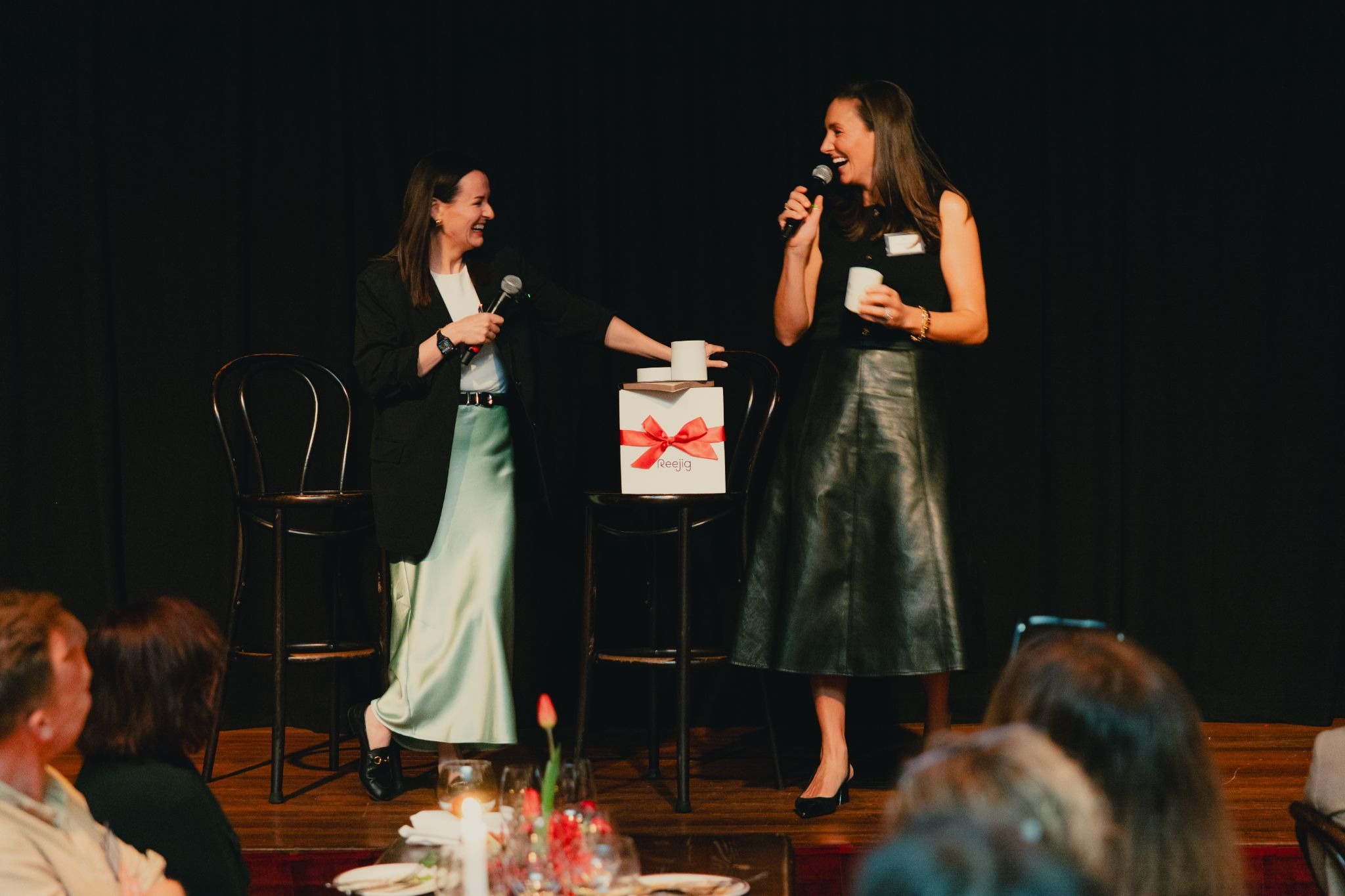 Siobhan Savage and Louisa Grundy on stage with microphones at the Reejig executive dinner.
